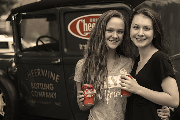 Two girls posing with cheerwine and antique car